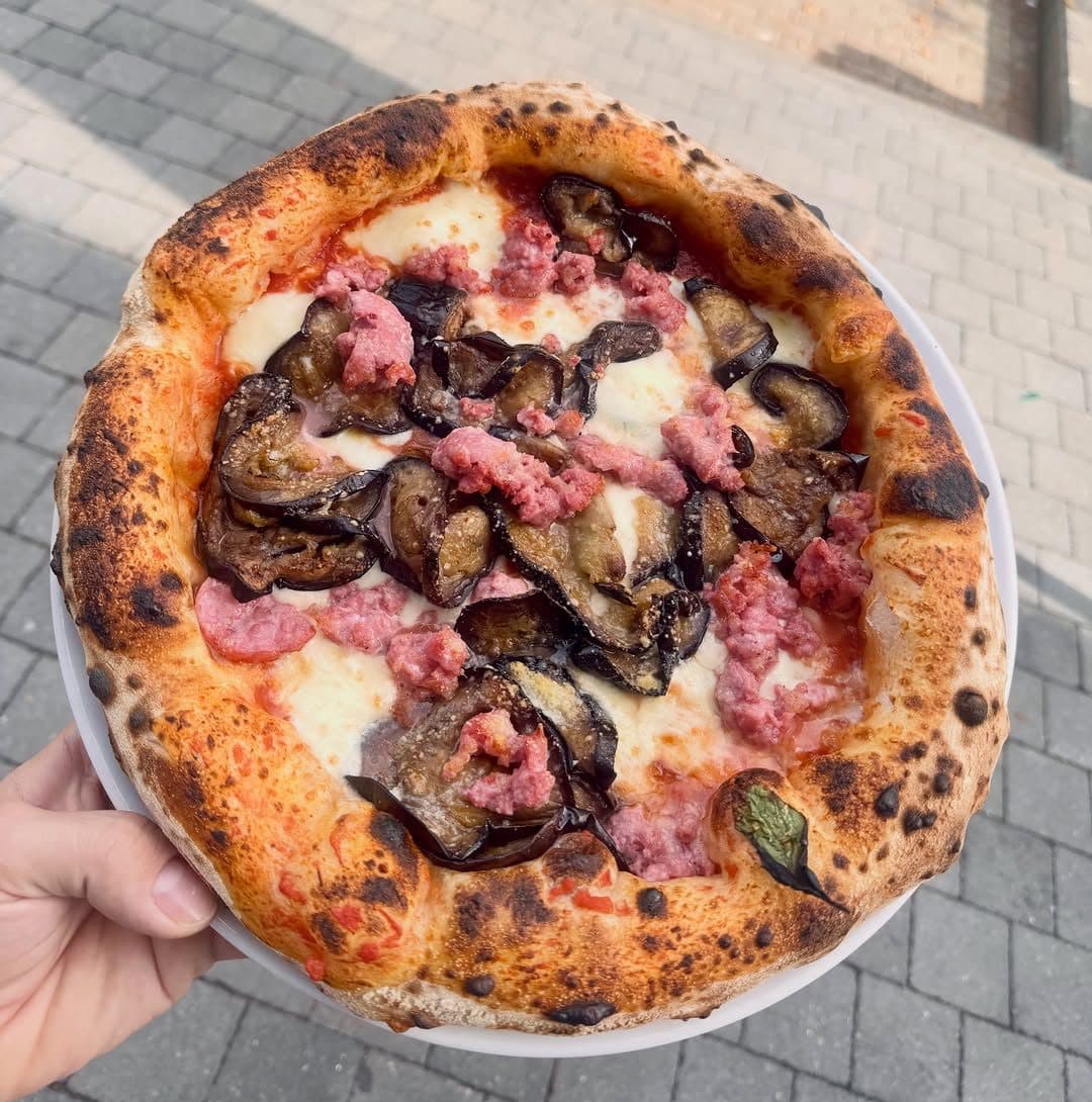 Pizza parmigiana, aubergines et saucisse, tenue au-dessus de la table